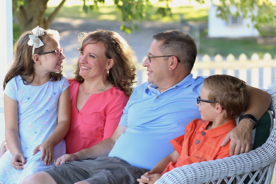 Daughter, mom, dad, and son sit together on a couch and laugh