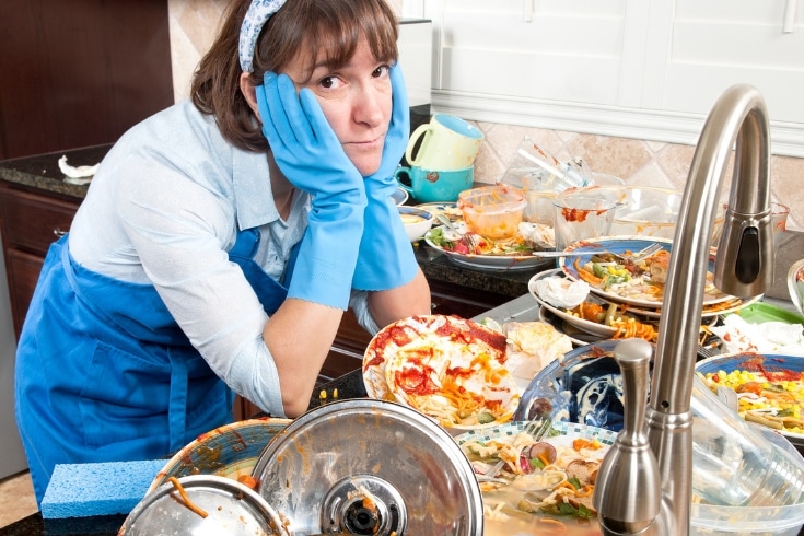 Overwhelmed woman stands by a counter filled with dirty dishes