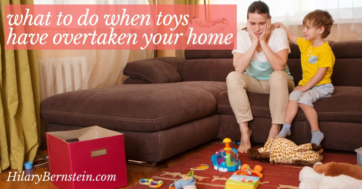 Mom sits on a couch with her head in her hands, frustrated by a mess of toys on the floor