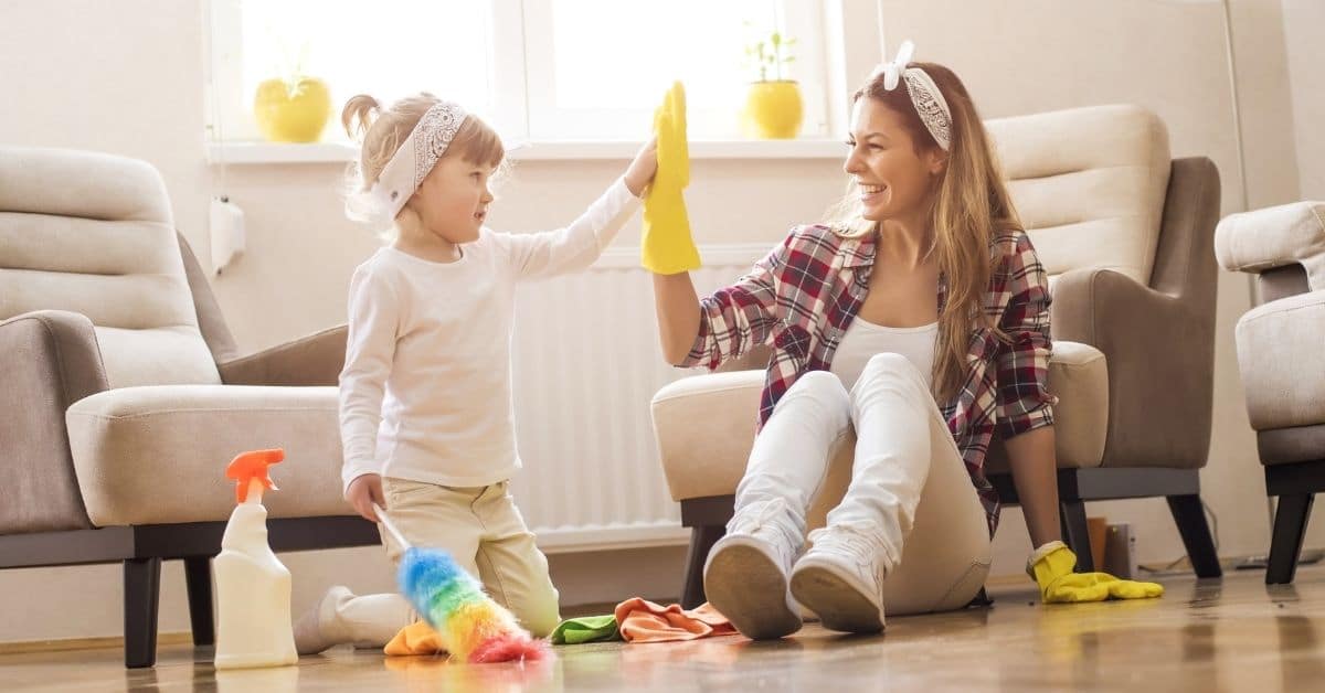 Young daughter and mother high five after dusting the living room
