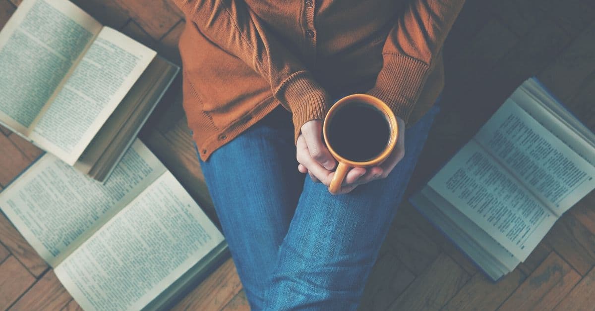 Woman sits on floor with coffee and books